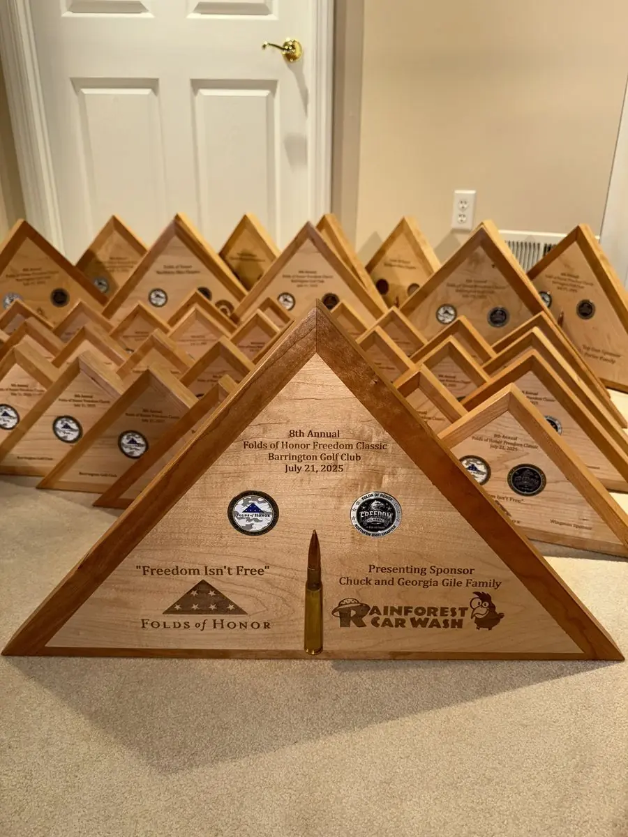 Dozens of triangular wooden flag cases lined up on a carpet, the front one engraved for an annual charity golf event