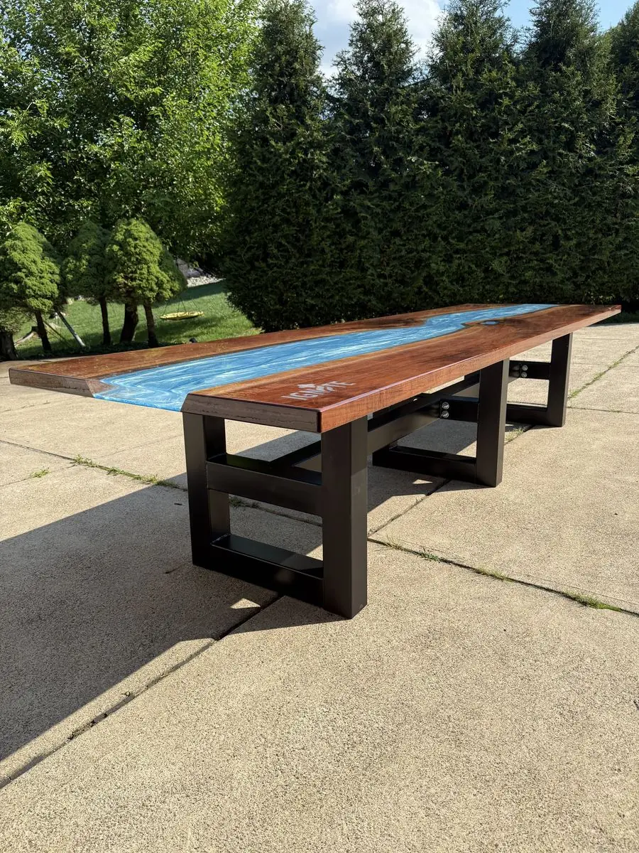 Long wooden table with a winding blue epoxy river down the middle and a black steel base, outdoors