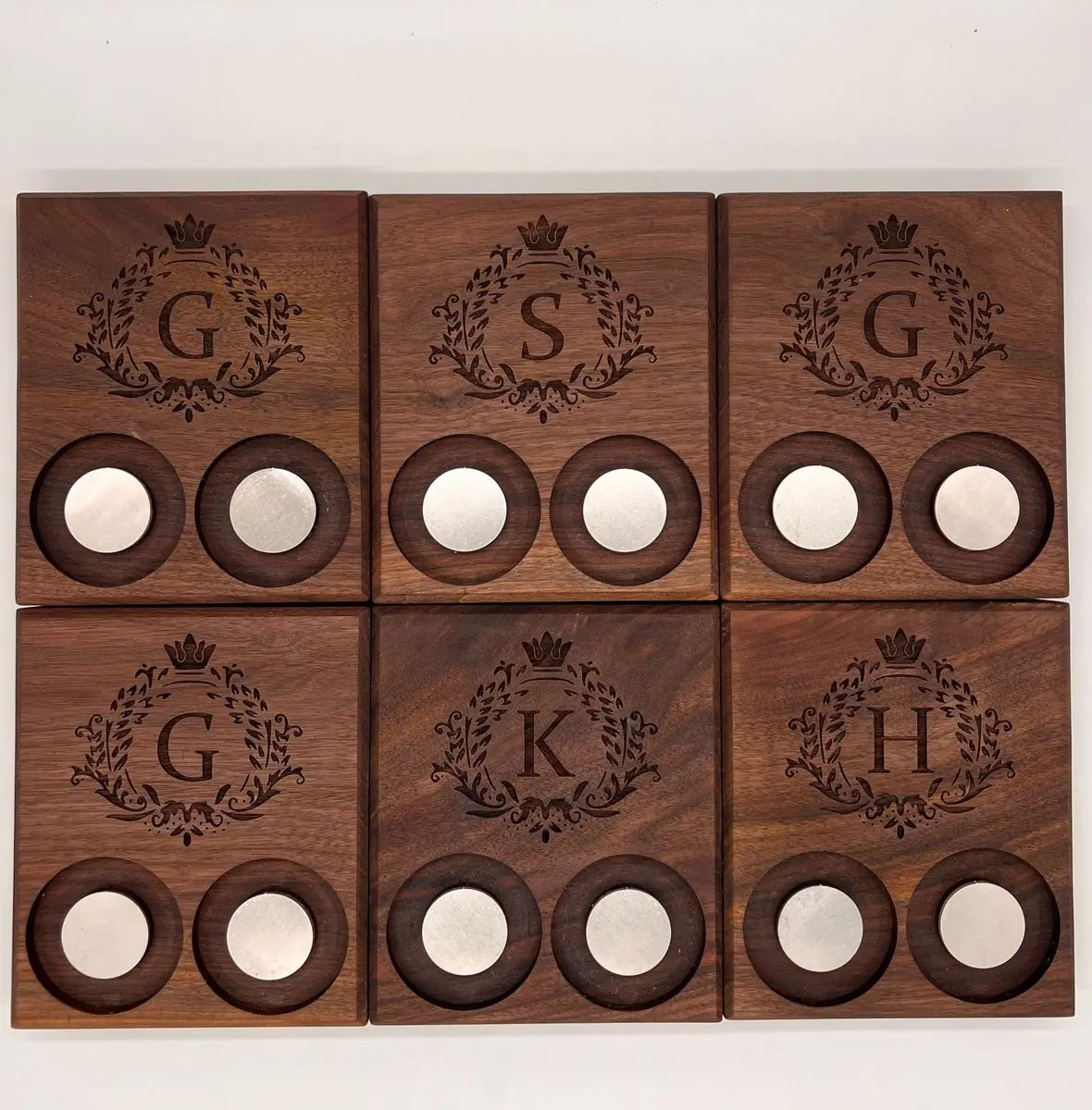 Six dark wood trays, each engraved with a crowned laurel wreath monogram and holding two round metal discs in recessed circles