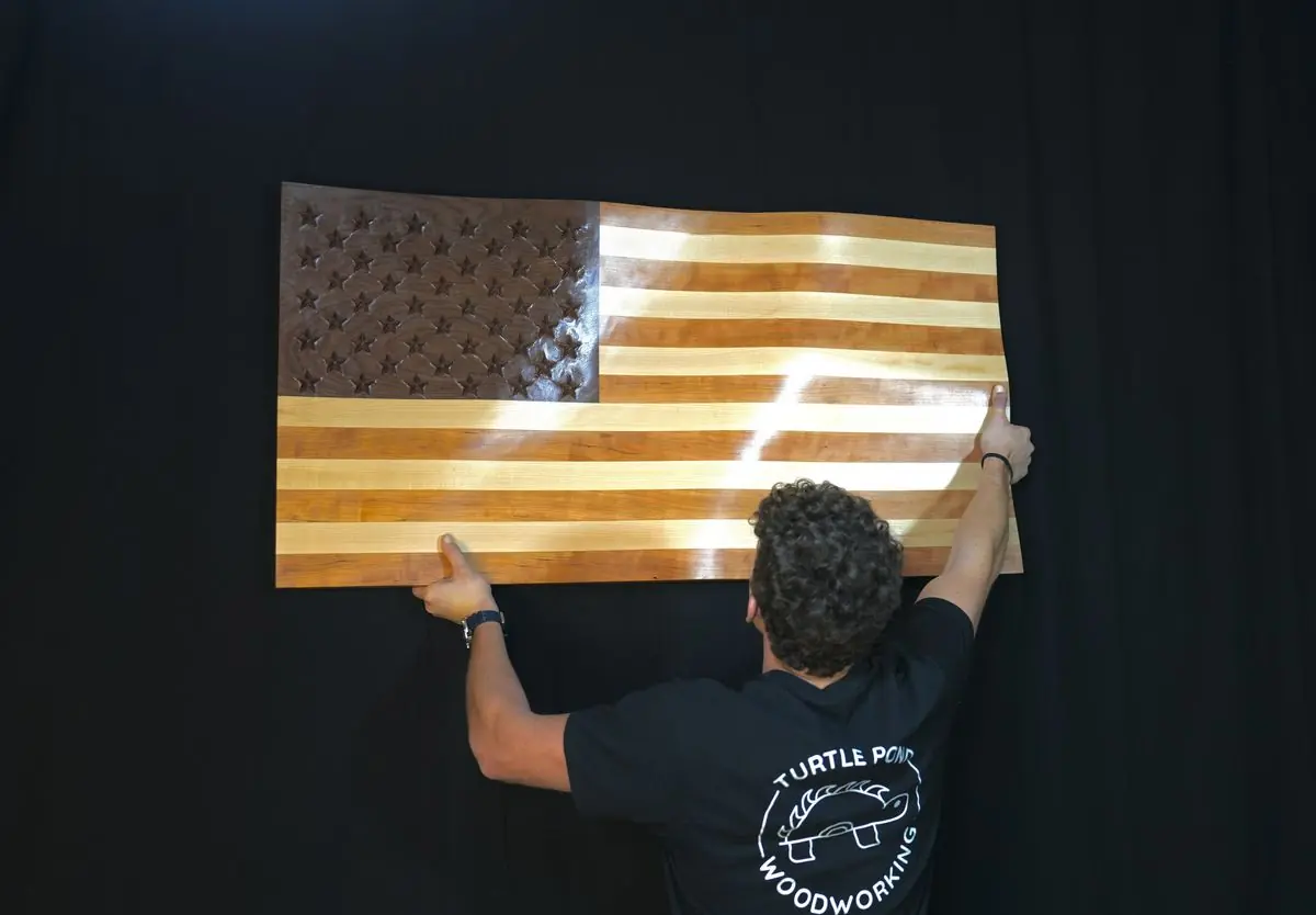 Someone in a Turtle Pond Woodworking shirt lifting the wooden flag onto a wall