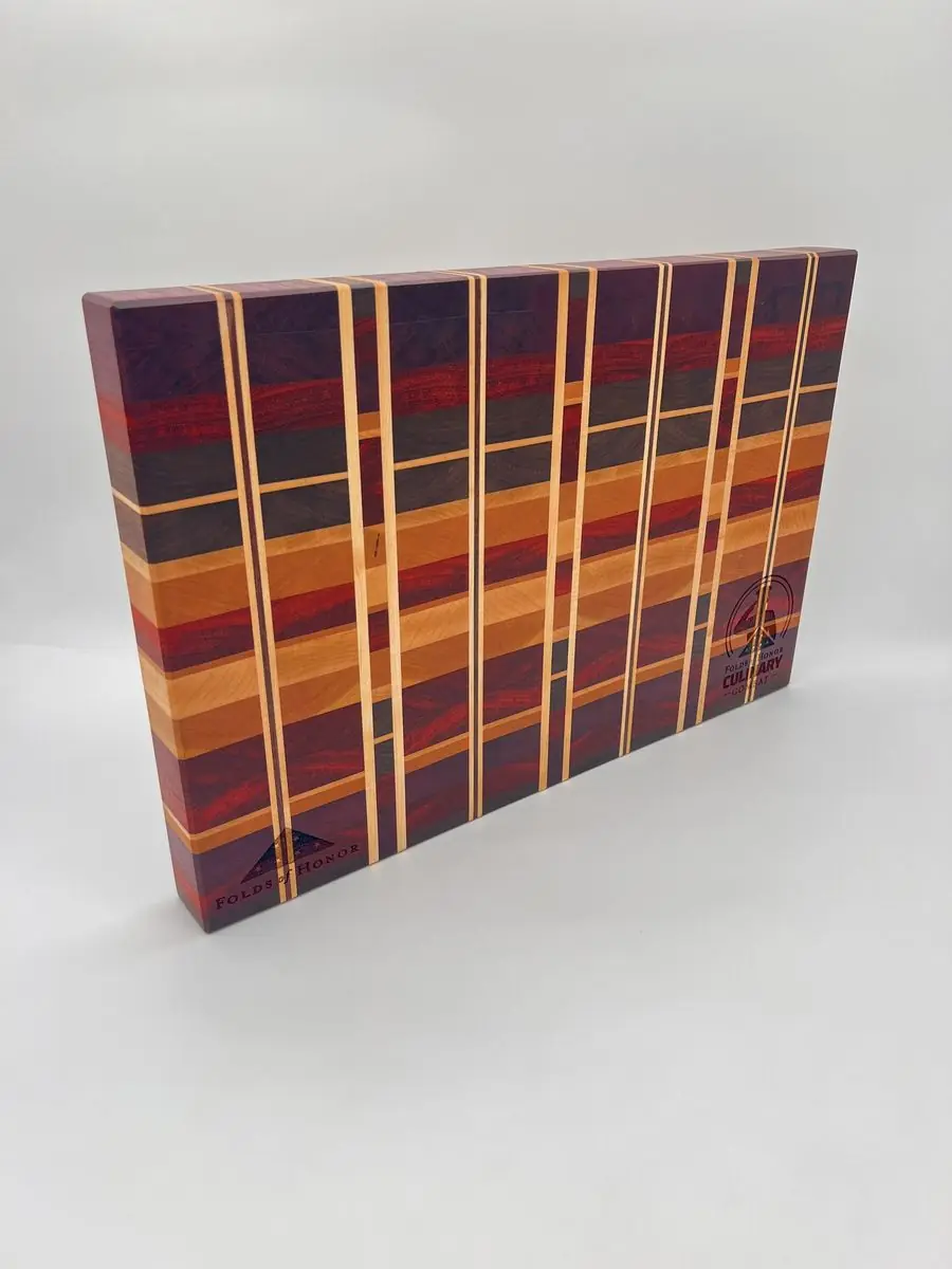 Striped end-grain cutting board in red, orange, purple and dark woods, standing on edge at an angle