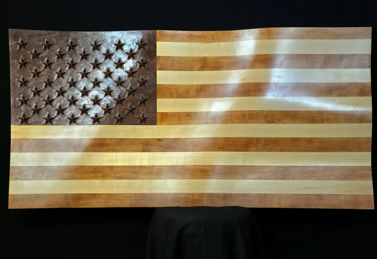 Wooden American flag with alternating light and dark wood stripes and carved stars in the blue field